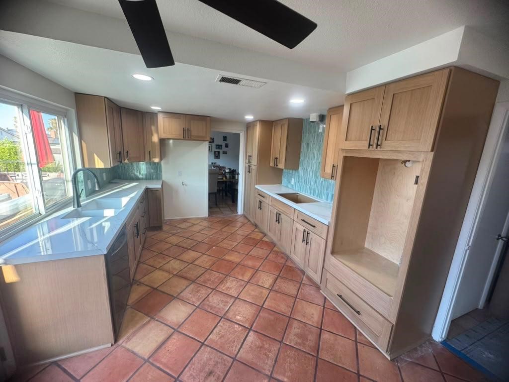 Kitchen remodel with light wood cabinets, terracotta tile floor, and teal backsplash