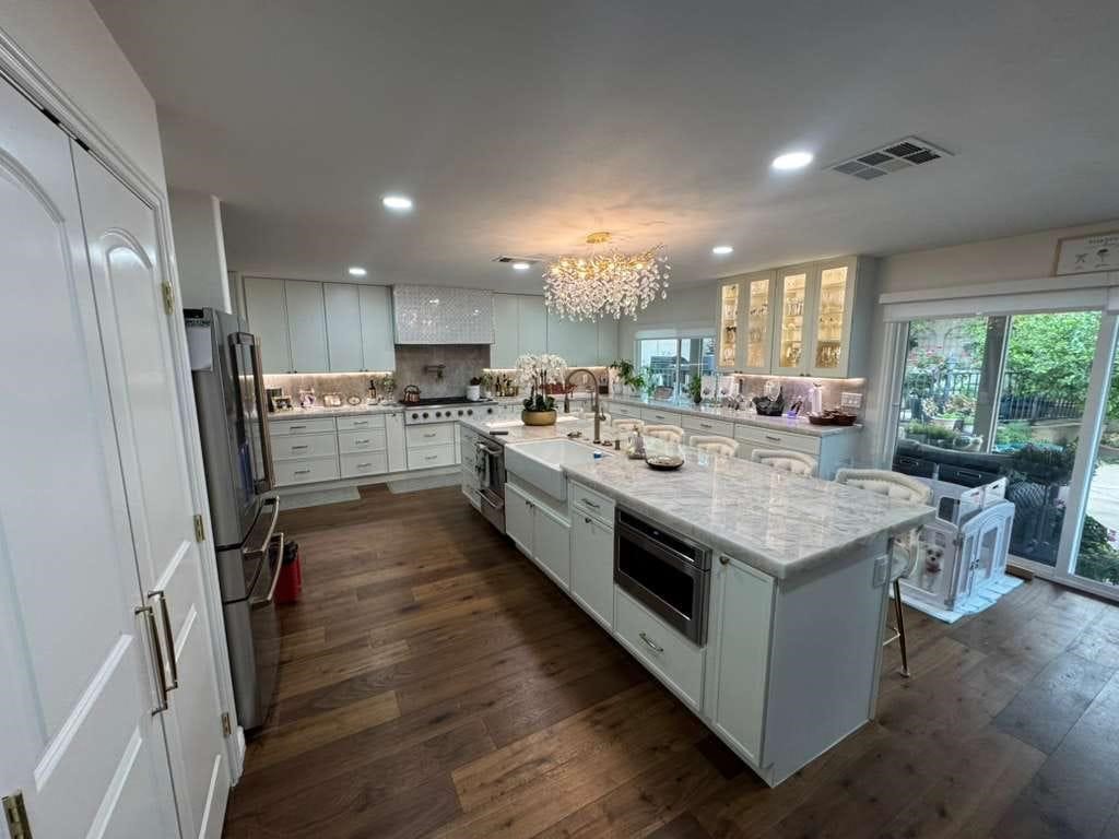 Large white kitchen remodel with marble island, chandelier, and hardwood floors